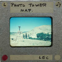 Old photograph of a film camera on a tripod with a scenic landscape behind it.