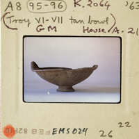 The image shows an ancient bowl with a handle, displayed against a white background.