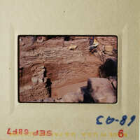 An archaeological site with stone structures, people working on excavation, and a dirt pathway.