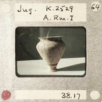 A photograph of a cracked clay pot with a label and number on it.