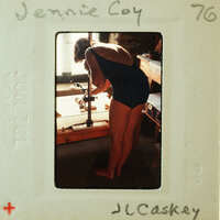 Woman wearing a swimsuit, bending over and working on something with her hands.