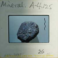 A photograph of a dark, metallic-looking rock on a white background with measurement marks around it.