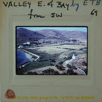 This is a vintage photograph of a valley with mountains and a body of water, enclosed within an old film negative frame.