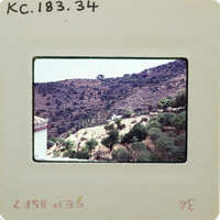 The image shows a photograph of a mountainous landscape with trees and shrubs, displayed on an old-fashioned film strip.