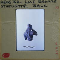 A small, dark-colored artifact on display with a label and identification number.