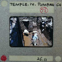 A photograph of archaeologists working at a site with water on the surface of the trench.