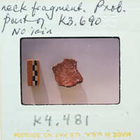 A photograph of a small, brown object with a label and handwritten notes on the border.