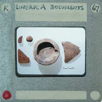 A small, broken clay pot with fragments on a display card.