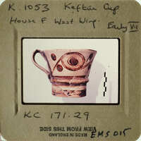 A photograph of an ancient Greek cup with intricate designs, displayed on a card.