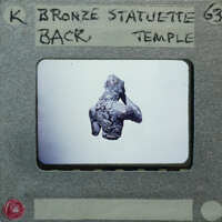 Small bronze statue of a figure with hands raised, from behind displayed on a white surface.