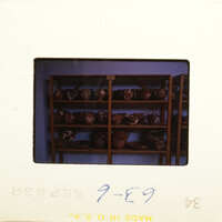 Photograph of pottery on shelves with blue writing on white background.
