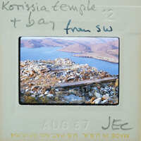 A vintage photograph of a rocky outcrop overlooking a body of water, with mountains in the background.