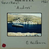 Old photograph of a coastal town with a ship on the water, labeled "Andros" and signed by E. Milburn.