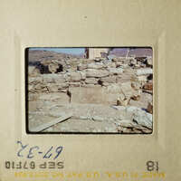 The photo shows an ancient stone structure, possibly ruins, with rubble scattered around and a clear sky above.