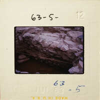 A photograph of an old stone structure with visible erosion and damage, possibly a bridge or wall.