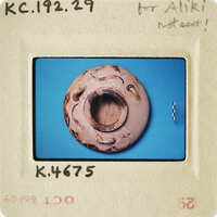 Small clay object with hole, photographed on blue background.