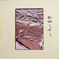 Photograph showing an aerial view of a rocky landscape with patches of dirt and vegetation, captured on an old film slide.