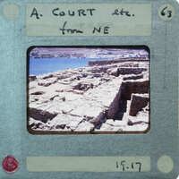 A vintage photograph of a stone structure, possibly ruins, with water and sky in the background, displayed on an old-fashioned film strip.