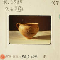 Ancient ceramic pot with visible cracks and imperfections, resting on a surface.