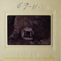 This is a photograph of an old slide showing a small cave entrance with rocks around it.