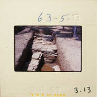 Stone-lined waterway with vegetation and trees in background.