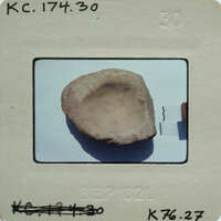 A photograph of a small, round, light-colored plaster fragment with a hole in the center.