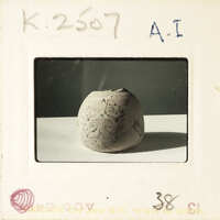 A small, round clay pot with intricate designs on a white surface.