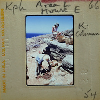 Two people working on a stone wall near the ocean with blue sky and clear weather.
