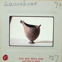 A small, dark brown clay pot with a handle and spout on a white surface.