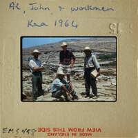 Four men standing together, smiling, with mountains and ruins in the background.