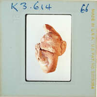 A photograph of a small, crudely made clay figurine resembling a human head with ears and facial features.