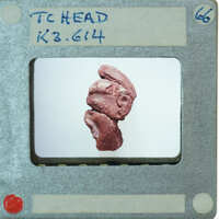 A close-up photograph of a small red figurine with a face, displayed on a white background.