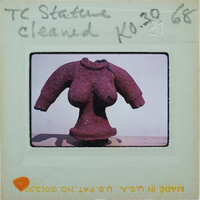 The image features a unique sculpture of a woman's torso made from red beads, displayed on a stand against a white wall.