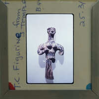 Ancient clay figurine of a humanoid form with detailed markings, displayed on a card within an envelope.