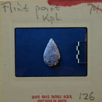 An ancient flint tool with a pointed tip, photographed on a blue background.