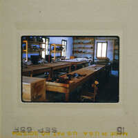 An old photo of a workshop with wooden tables and shelves filled with various tools and equipment.