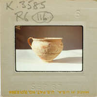 Cracked ceramic cup with painted decorations and a handle on a table.