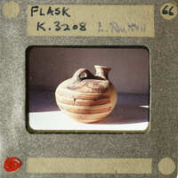 A photograph of an ancient Greek vase with a black figure and red stripe pattern.