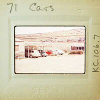 Old photo of a car lot with several parked cars on a dirt ground.