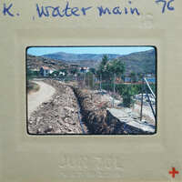 A photograph of a dirt road with mountains and houses in the background, on an old film strip.