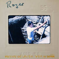 Man holding a ladder near a cave entrance.