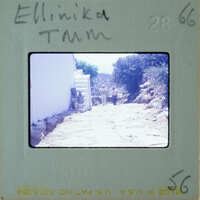 A photograph of a narrow, rocky street with two people and white buildings on the sides.