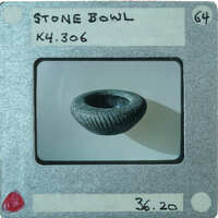 A photograph of a small stone bowl with diagonal incised lines from the side.
