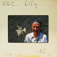 A woman holding a flower, smiling at the camera.