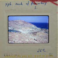 Photo of a rocky coastline with blue water and sky, on a film strip labeled "KPH".