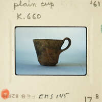 Ancient-looking clay cup with handle and spout on a plain background.