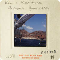 A photograph of a boat on water with mountains and houses in the background, taken from an elevated perspective.