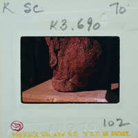 A photograph of a red clay pot with a handle, taken from above and placed on a wooden surface.