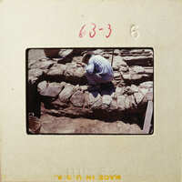 Man kneeling down next to rock wall under construction.