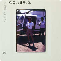 Two people standing next to a helicopter, with one man posing and the other looking on.